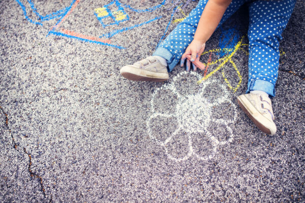 Close up of little girl in canvas shoes drawing with chalks on the sidewalk